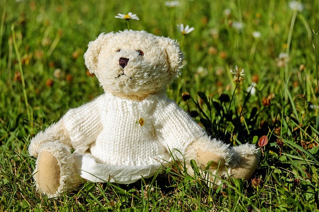 A knitted teddy bear sitting in grass among daisies.