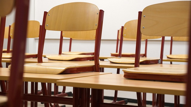 Rows of empty wooden chairs and desks in a classroom.